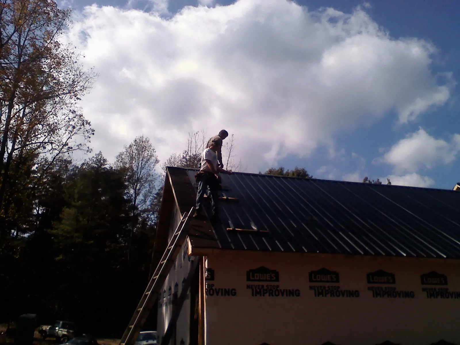 Roofer fastening dark metal panels high against a cloudy sky, from a Roof Inspection job in Stockdale